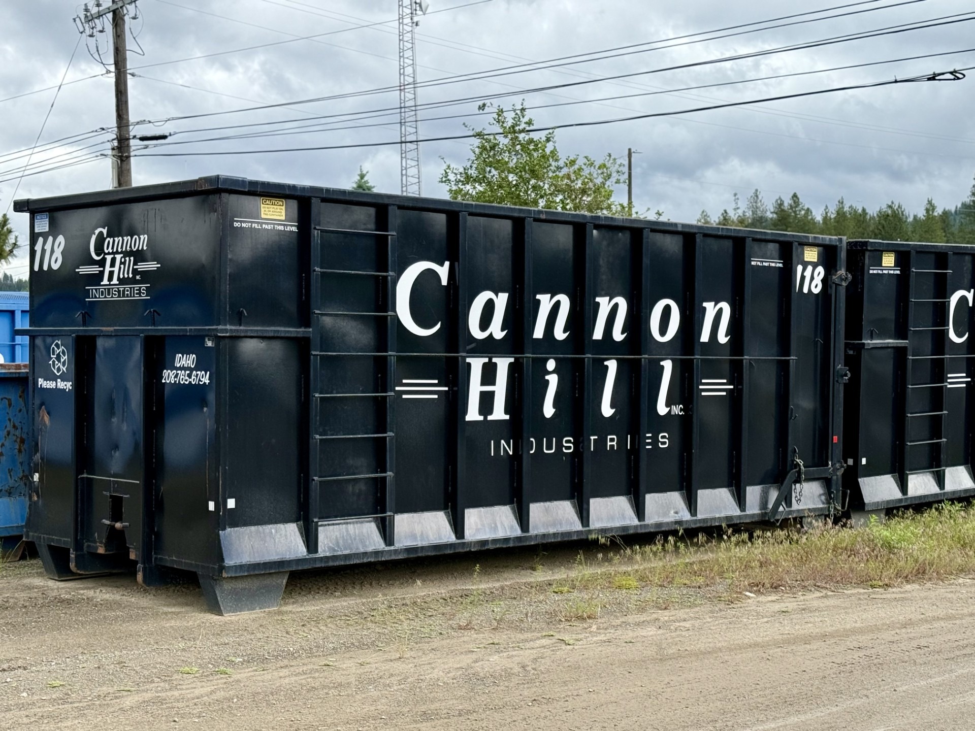 Cannon Hill Industries waste container labeled "118." The container is prominently marked for recycling, positioned outdoors among utility poles.