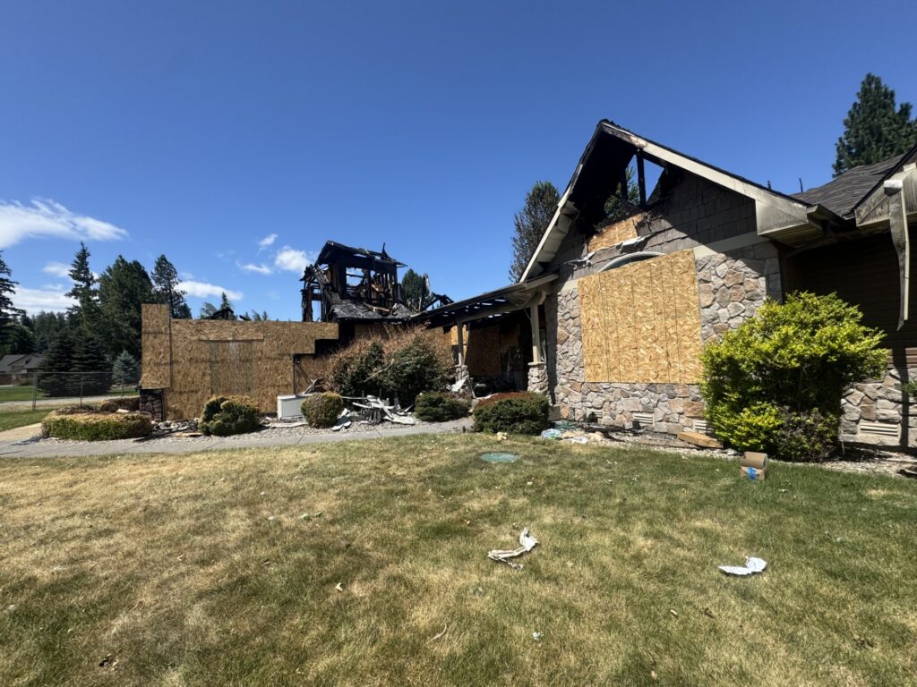 Burned house with boarded windows and a charred roof, situated in a suburban area. The image illustrates the aftermath of a fire disaster.